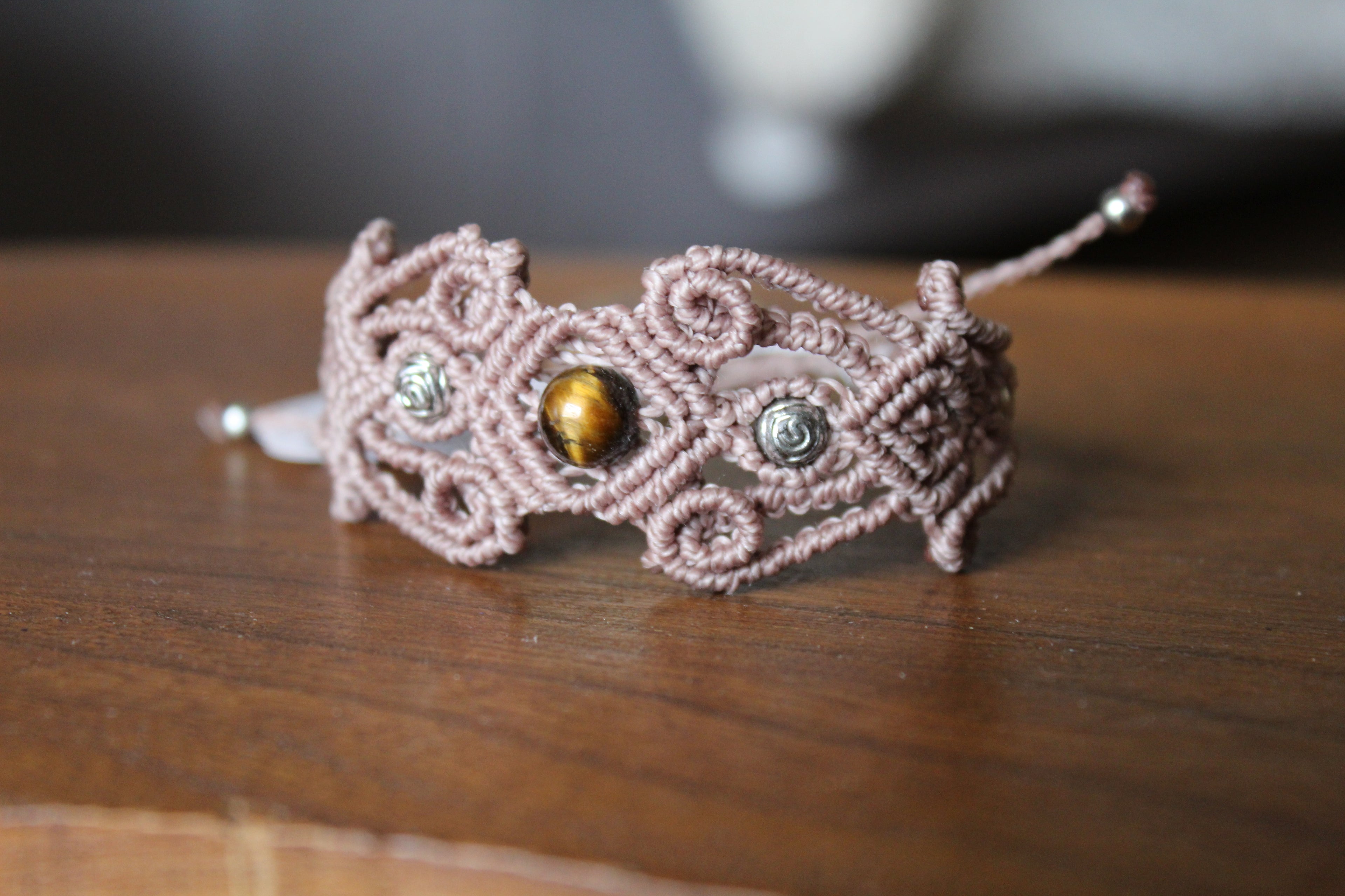 bracelet modèle @lesfilsambulants tisé a la main en micro macramé de couleur taupe et une perle en oeil de tigre.